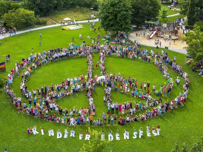 Menschengruppe steht in Form eines Friedenssymbols auf einer Wiese