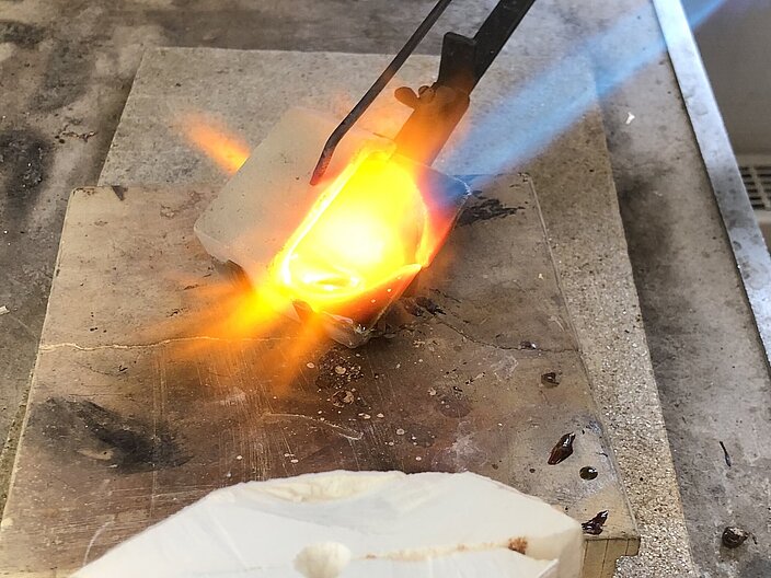 Glas wird in der Technik "Ossa-Sepia-Guss" auf einer Arbeitsfläche durch Brenner erhitzt. 
