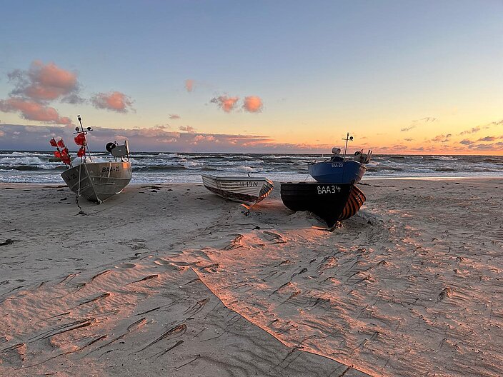 07_Küstenfischerei_Boote_am_Außenstrand_von_Baabe_Thomas_Neuss Vier Boote am Außenstrand von Baabe liegen im Sand. Im Vordergrund ein in Klinkerbauweise gebautes Holzboot, mittig ein Kunststoffboot aus skandinavischer Serienproduktion, links und rechts zwei nach Vorgaben der Fischer gebaute Aluminiumboote.