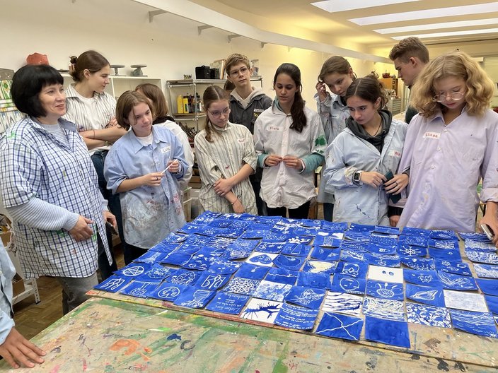 Ukrainische Schüler und Schülerinnen stehen um einen Tisch herum und schauen auf die in einem Kunstworkshop kreierten Blaudrucke.