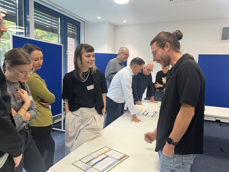 Gruppenarbeit Konferenz zur Lehrkräftebildung Mehrere Menschen stehen um einen Tisch herum und blicken auf die dort ausgelegten Dokumente.