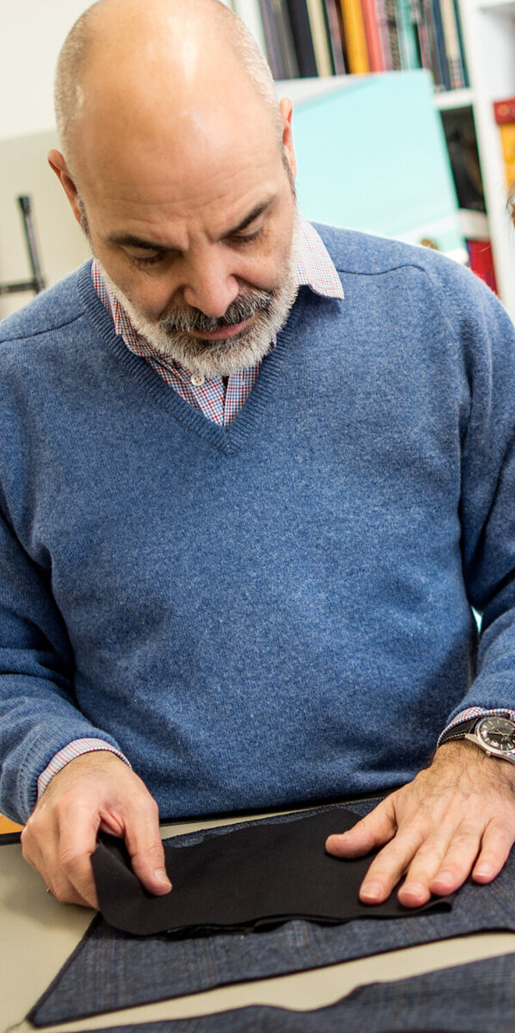 Zwei Personen (Auszubildendende und Lehrer) arbeiten gemeinsam an einem Stoffst&uuml;ck, das vor ihnen auf einem Tisch liegt