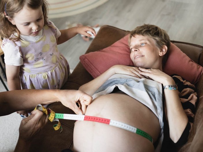 Eine Hebamme untersucht eine schwangere Frau unter den Augen der Tochter