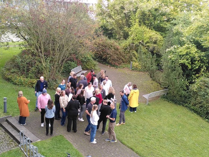 Blick von oben auf eine Gruppe von Menschen in einem Innenhof, die als Gruppe beieinander stehen.