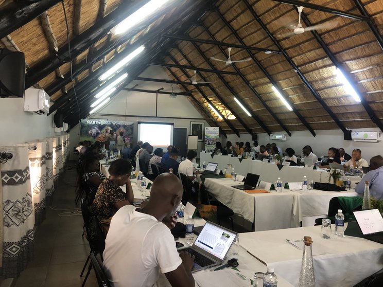 Workshop_Zimbabwe_BRManagement Ein großer Konferenzsaal mit vielen Teilnehmenden, die in einer U-Form um Tische sitzen.