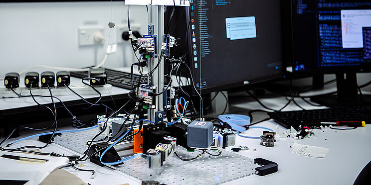 Robotik Schreibtisch mit verschiedenen wissenschaftlichen Geräten und Computerbildschirmen, die einen Robotik-Aufbau zeigen