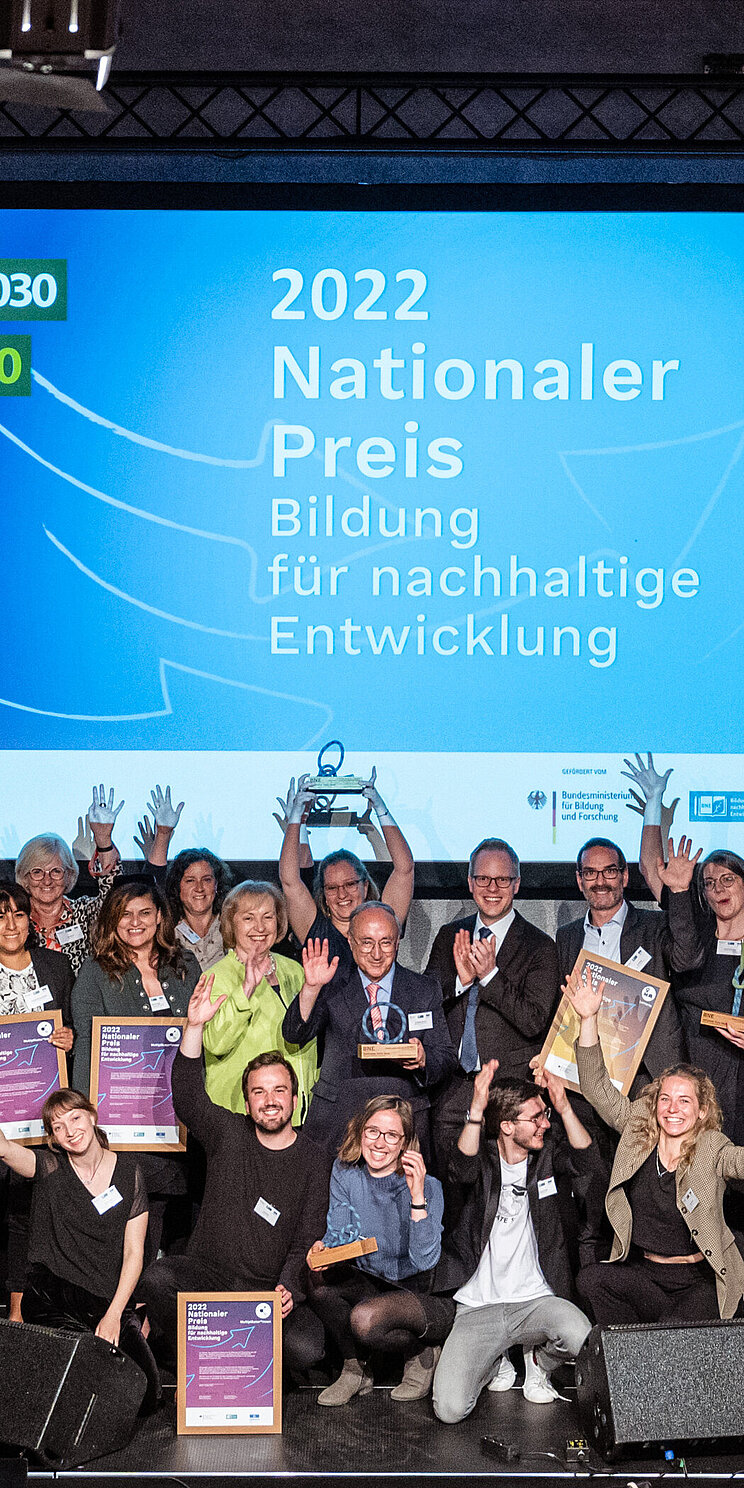Preistragende 2022 AUf diesem Foto sind die jubelnden Preistragenden des BNE-Preises 2022 auf der Bühne zu sehen. Sie halten ihre Urkunden und Trophäen in den Händen