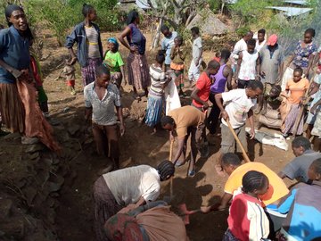 Dorfbewohner sanieren die Terrassen, indem sie zunächst die Erde ebnen. Sie stehen in einer Gruppe zusammen, während einige mit Werkzeugen die Erde glätten. 