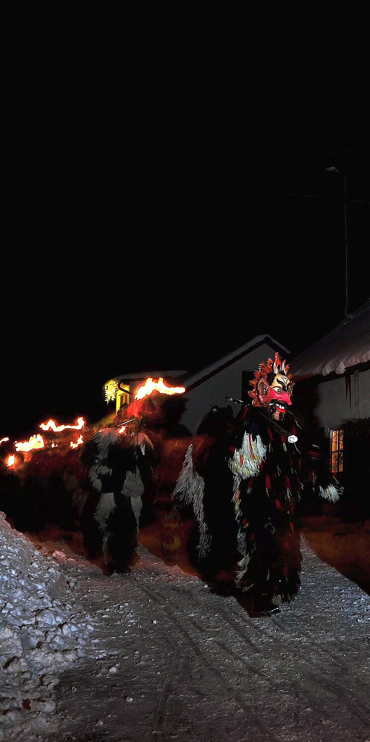 Spitze des Perchtenzuges mit Köstümen, Masken, Trommeln und Fackeln vor einem Haus in Kirchseeon.