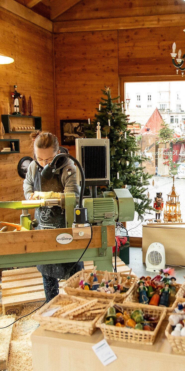 Zwei junge Menschen arbeiten in einer weihnachtlich geschmückten Schauwerkstatt an Holzspielzeugen.
