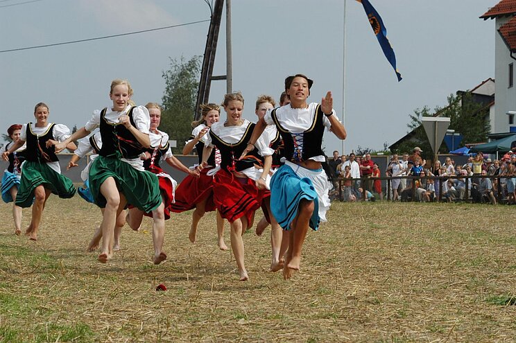 Frauen in Tracht rennen barfuß über eine Wiese