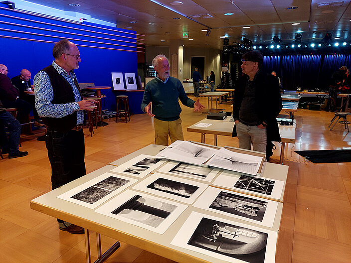 Schwarz-Weiß Fotos liegen ausgebreitet auf einem Tisch im fineartforum.