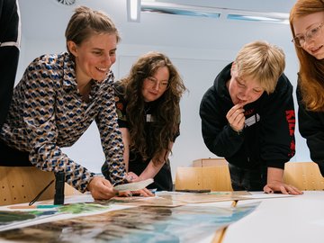 Vier Schülerinnen stehen mit einer Lehrerin um einen Tisch herum und schauen auf eine Landkarte.