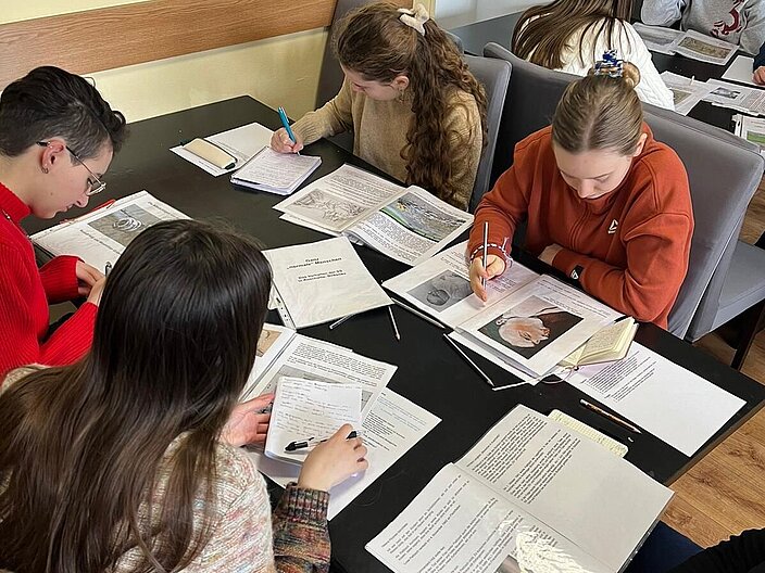 An zwei Tischen sitzen 6 Schüler*innen und studieren Dokumente zur Vorbereitung des Besuches in Auschwitz.