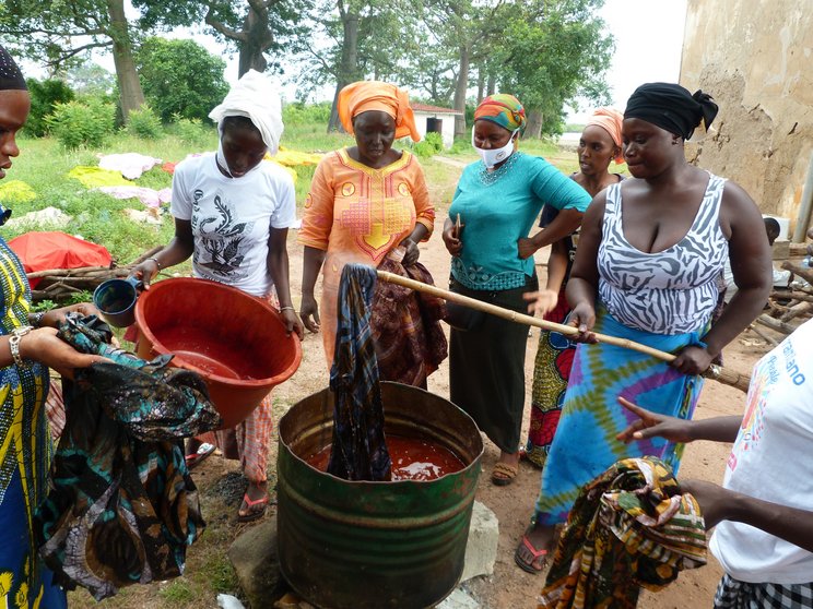 #SOS2020_Gambia_Women_Heritage_c_NCAC Frauen betreiben Batikkunst in Gambia. Sie tauchen Tücher in eine rote Flüssigkeit.