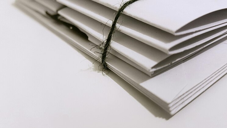 Stapel Papierakten Ein dünner Stapel Papierakten, der mit einer grünen Korden zusammengebunden wurde. Die Perspektive ist von schräg unten auf die auf einer Fläche liegenden Unterlagen.