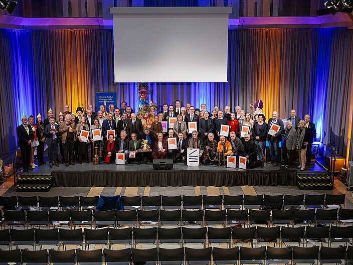 Perspektive in den Festsaal. Alle Urkundenträger:innen gemeinsam auf der Bühne.