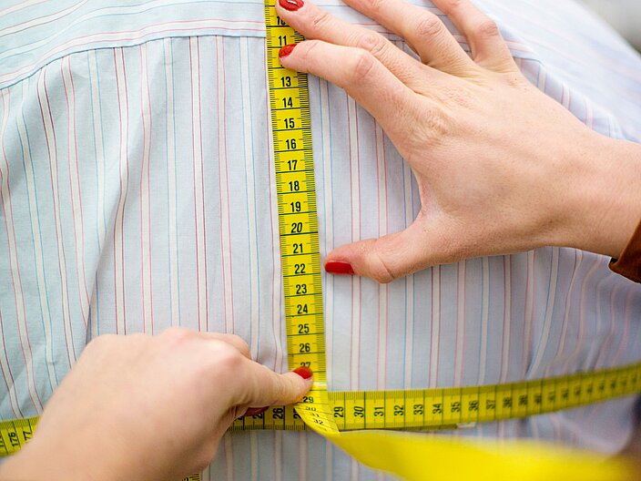 Person von hinten tr&auml;gt Hemd. Zweite Person f&auml;hrt mit einem Ma&szlig;band &uuml;ber den R&uuml;cken der hemdtragenden Person