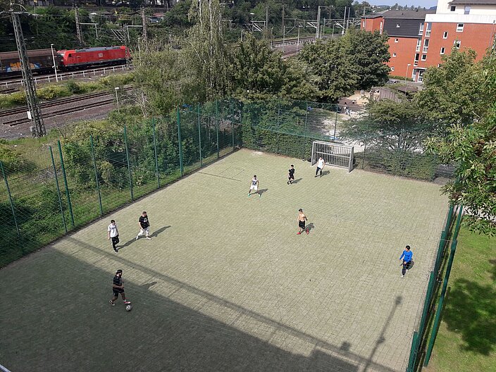 Vogelperspektive auf st&auml;dtischen Bolzplatz neben Bahngleisen. Eine Gruppe Jugendlicher spielt Ball auf ein Tor.