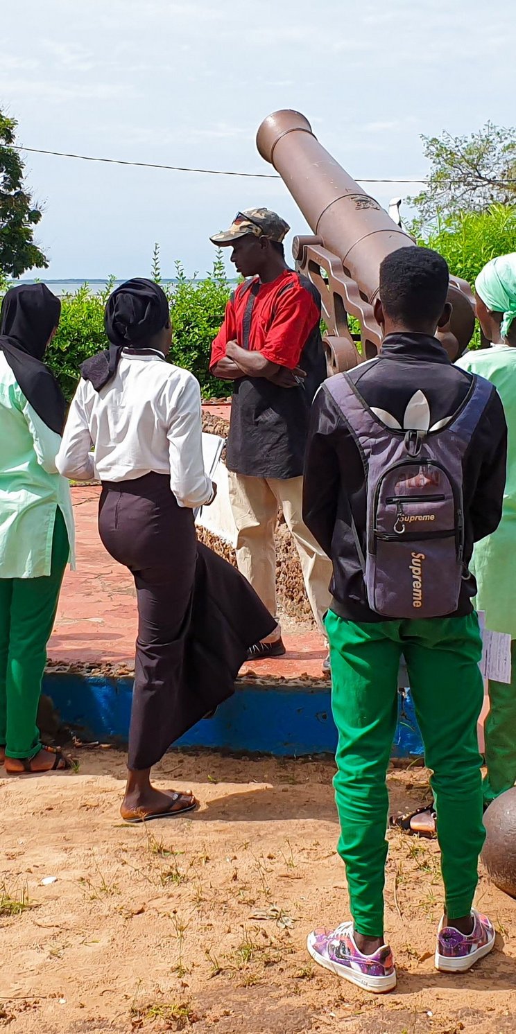 Schülerinnen und Schüler werden über das Welterbe unterrichtet. Sie stehen in einer Gruppe vor einer Kanone und hören der lehrenden Person zu. 