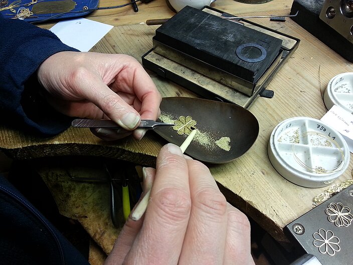 Mit den Händen wird an einer Goldblume gearbeitet mithilfe der Filigrantechnik, bei der das Staublot aufgelegt wird.