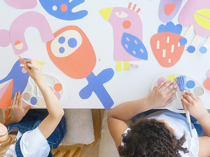 Zwei Mädchen im Kindergartenalter sitzen an einem Tisch und malen. Das Foto zeigt Sie aus der Vogelperspektive