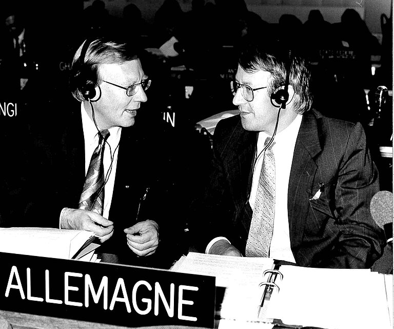 Schwarz-wei&szlig; Foto von Prof. Dr. Klaus H&uuml;fner und Wolfgang Reuther in einem Konferenzsaal, vor ihnen auf dem Tisch ein L&auml;nderschild "Allemagne"