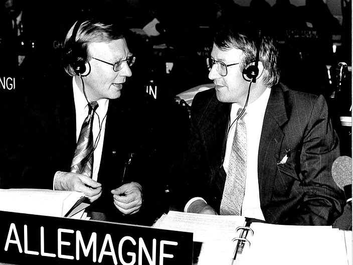 Schwarz-wei&szlig; Foto von Prof. Dr. Klaus H&uuml;fner und Wolfgang Reuther in einem Konferenzsaal, vor ihnen auf dem Tisch ein L&auml;nderschild "Allemagne"