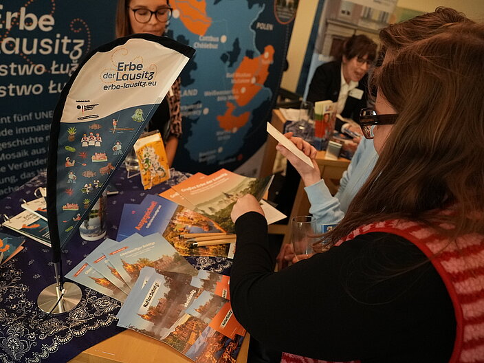 mehrere Personen stehen an einem Informationsstand mit Brosch&uuml;ren zum Projektverbund "Erbe der Lausitz"