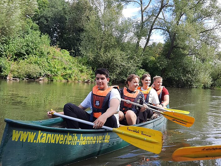 Vier ukrainische Schüler*innen sitzen im einem Kajak und paddeln auf einem Fluss.