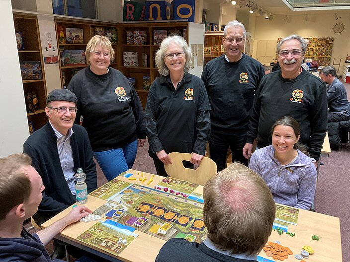 Ali Baba Spieleclub in Nürnberg. Ehrenamtliche Helfende als "Erklärbären" stehen gemeinsam vor Spieletisch.