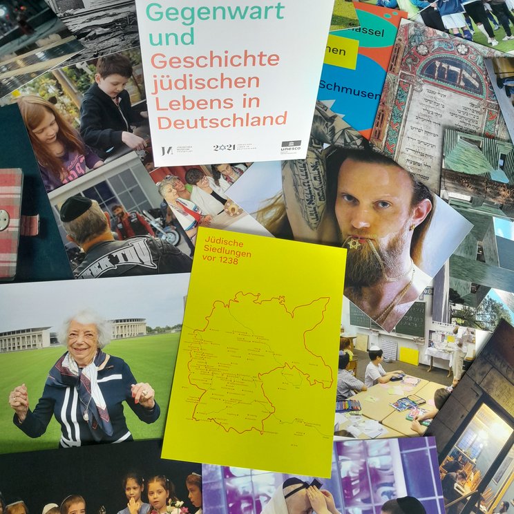 Eine Bilderkarten Box steht in der Mitte und herum liegen viele der einzelnen Bilderkarten mit verschiedenen Fotos zum jüdischen Leben in Deutschland, z.B. das Portrait einer Holocaustüberlebenden, Tattoos in hebräisch, beten etc.