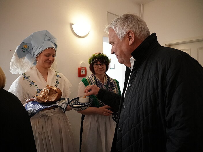 Zwei in sorbischer Tracht gekleidete Personen reichen den G&auml;sten Brot und Quark