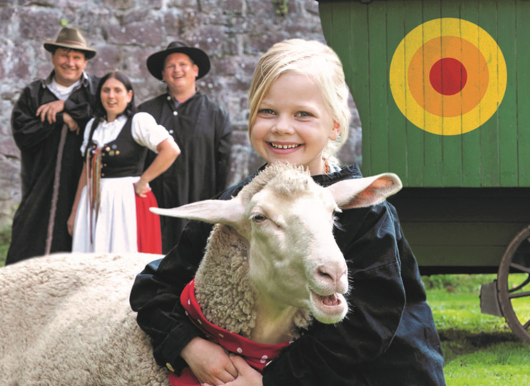 Jule_mit_Schaf_Cropped_Wolfgang_Schmidt Ein Kind umarmt ein Schaf. Im Hintergrund stehen drei Erwachsene in Tracht und blicken in die Kamera.