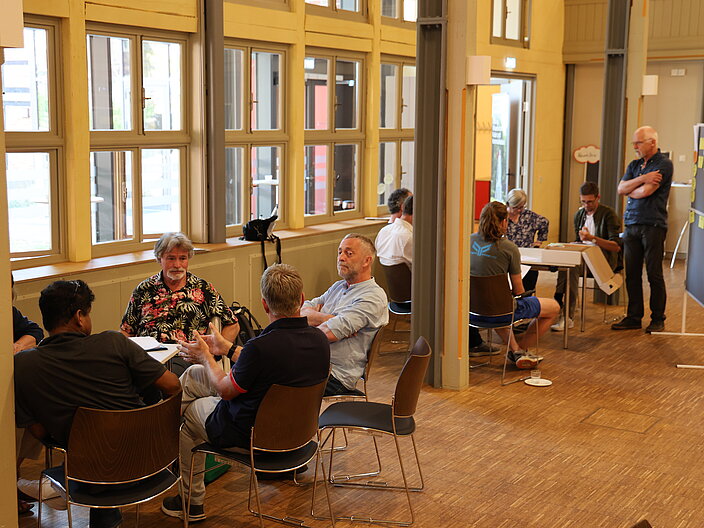 Zwei Themeninseln sitzen in Gruppen von f&uuml;nf Personen zusammen und sprechen miteinander.
