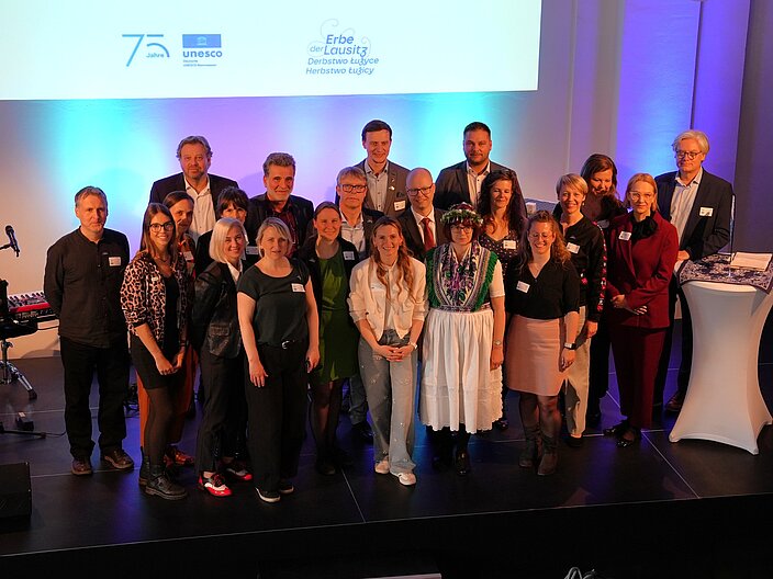 Gruppe an Menschen steht auf der B&uuml;hne bei der Regionalkonferenz