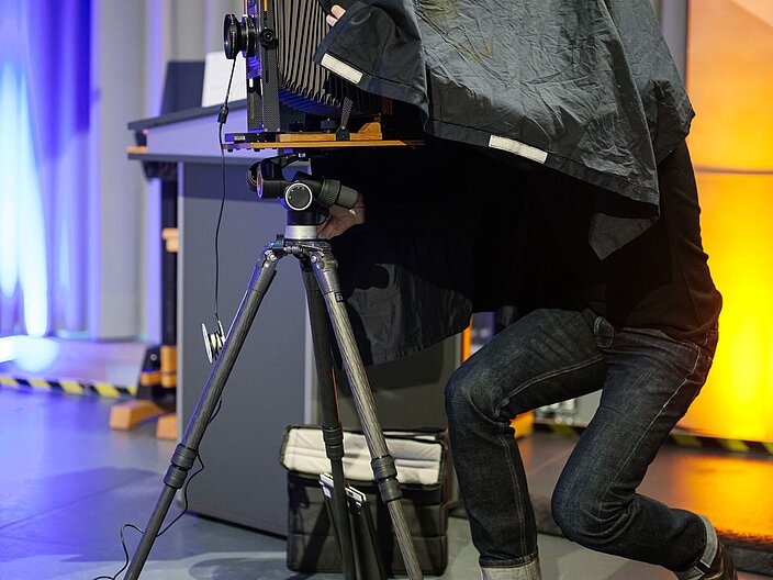 Urkundenverleihung_25_Fotografie Fotograf steckt unter einer Bedeckung und richtet das Gestell der Analogen Kamera ein.