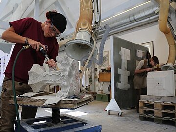 BAUHUETTE_Werkstatt_Bauhuette_Ulm_c_Katharina_Hild Handwerker bearbeitet einen behauenen Stein.