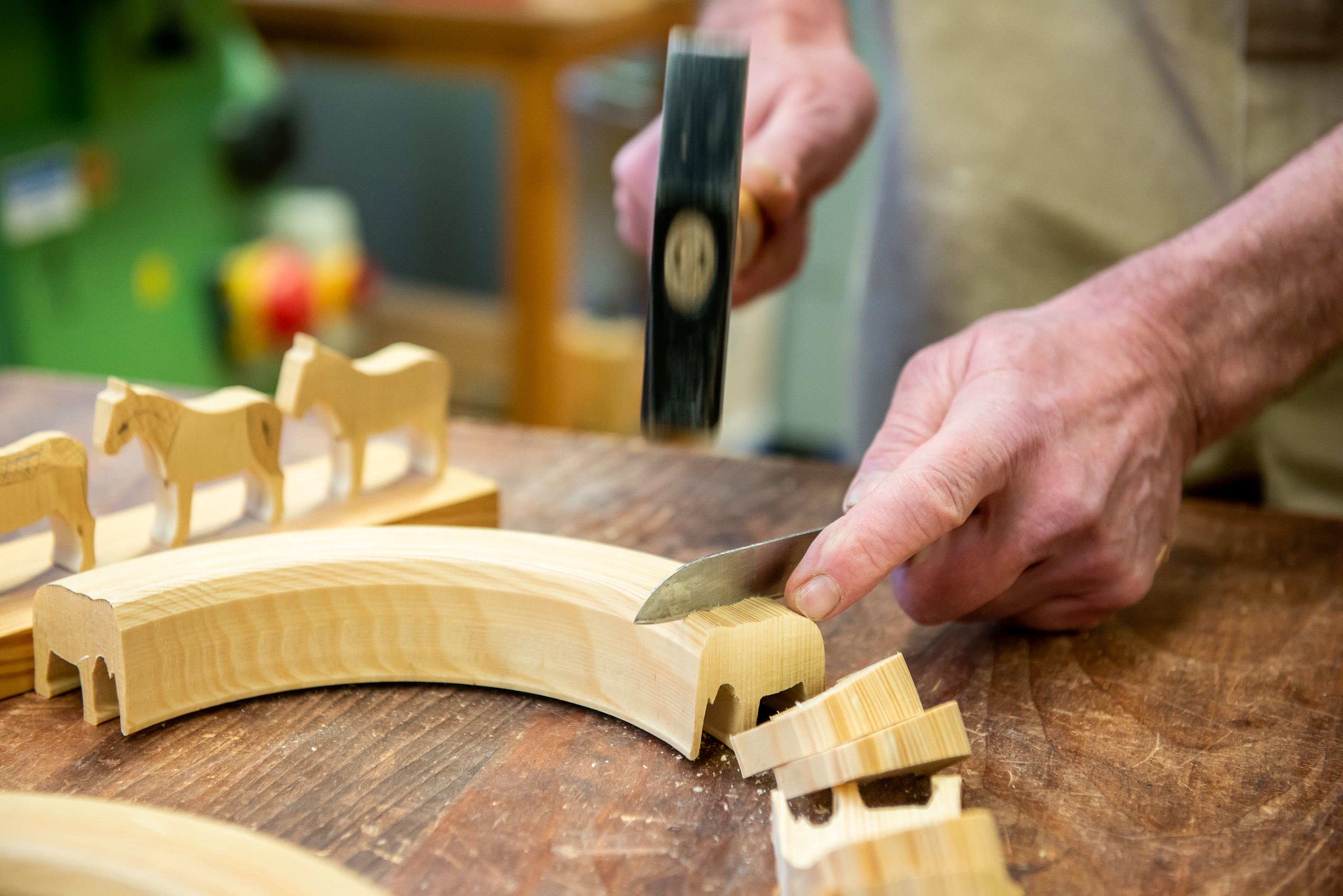 Mit einem Messer und Hammer werden aus einem Holzbogen Holzfiguren herausgebrochen.