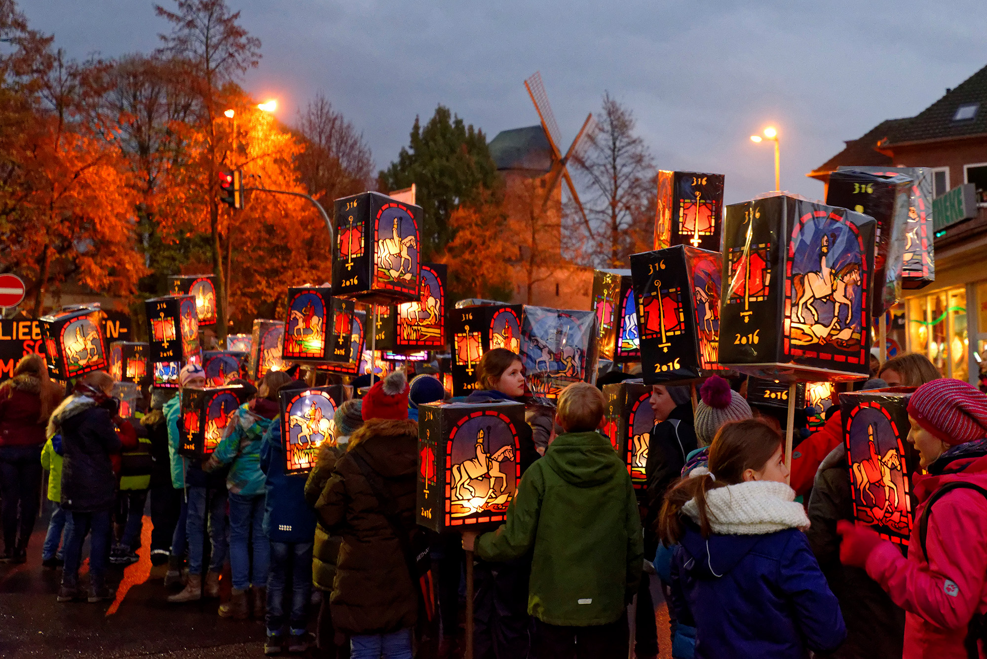 Kinder stehen auf der Stra&szlig;e im Halbdunklen und halten ihre Laternen in der Hand. Auf allen Laternen ist St. Martin auf einem Pferd abgebildet