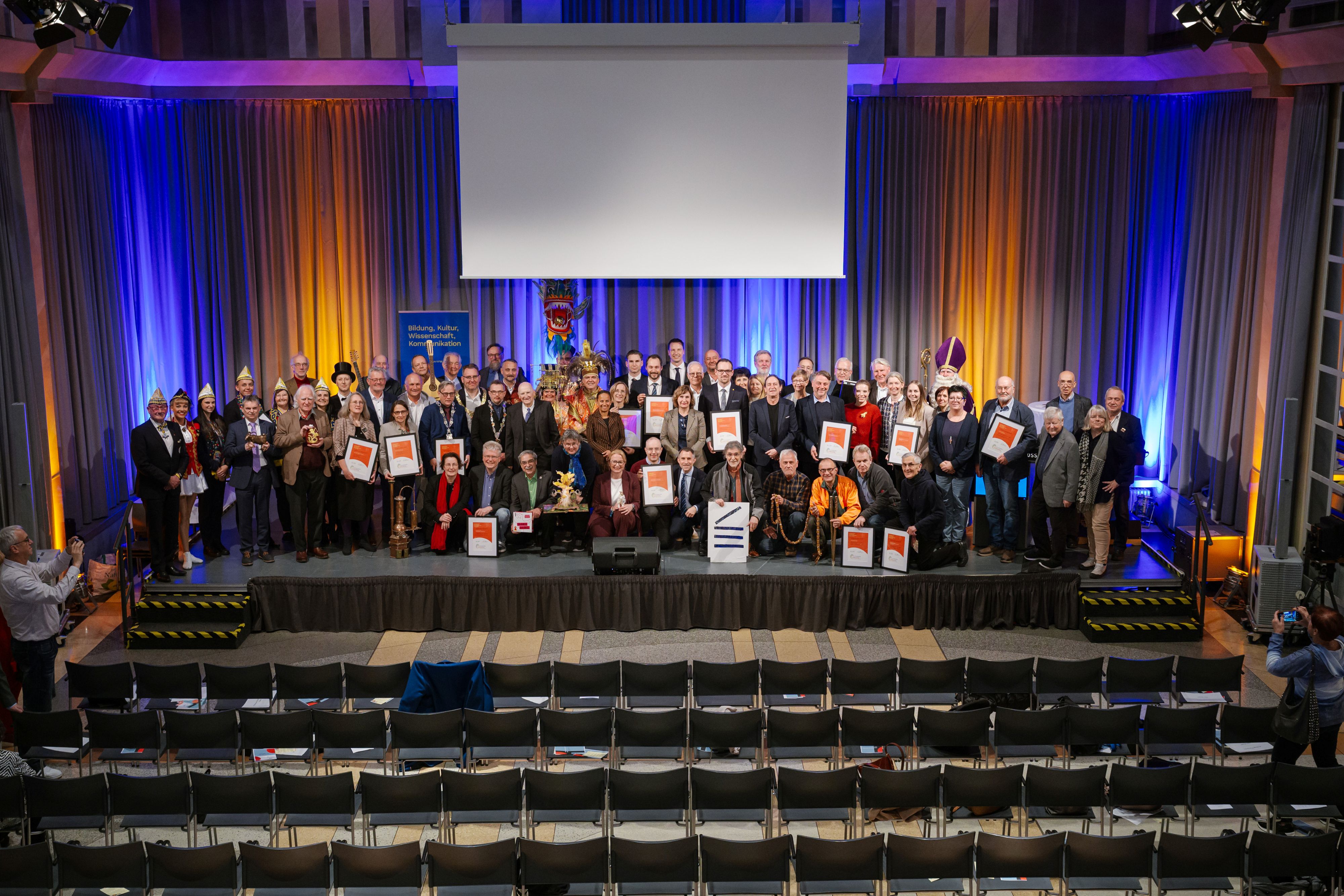 Perspektive in den Festsaal. Alle Urkundentr&auml;ger:innen gemeinsam auf der B&uuml;hne.
