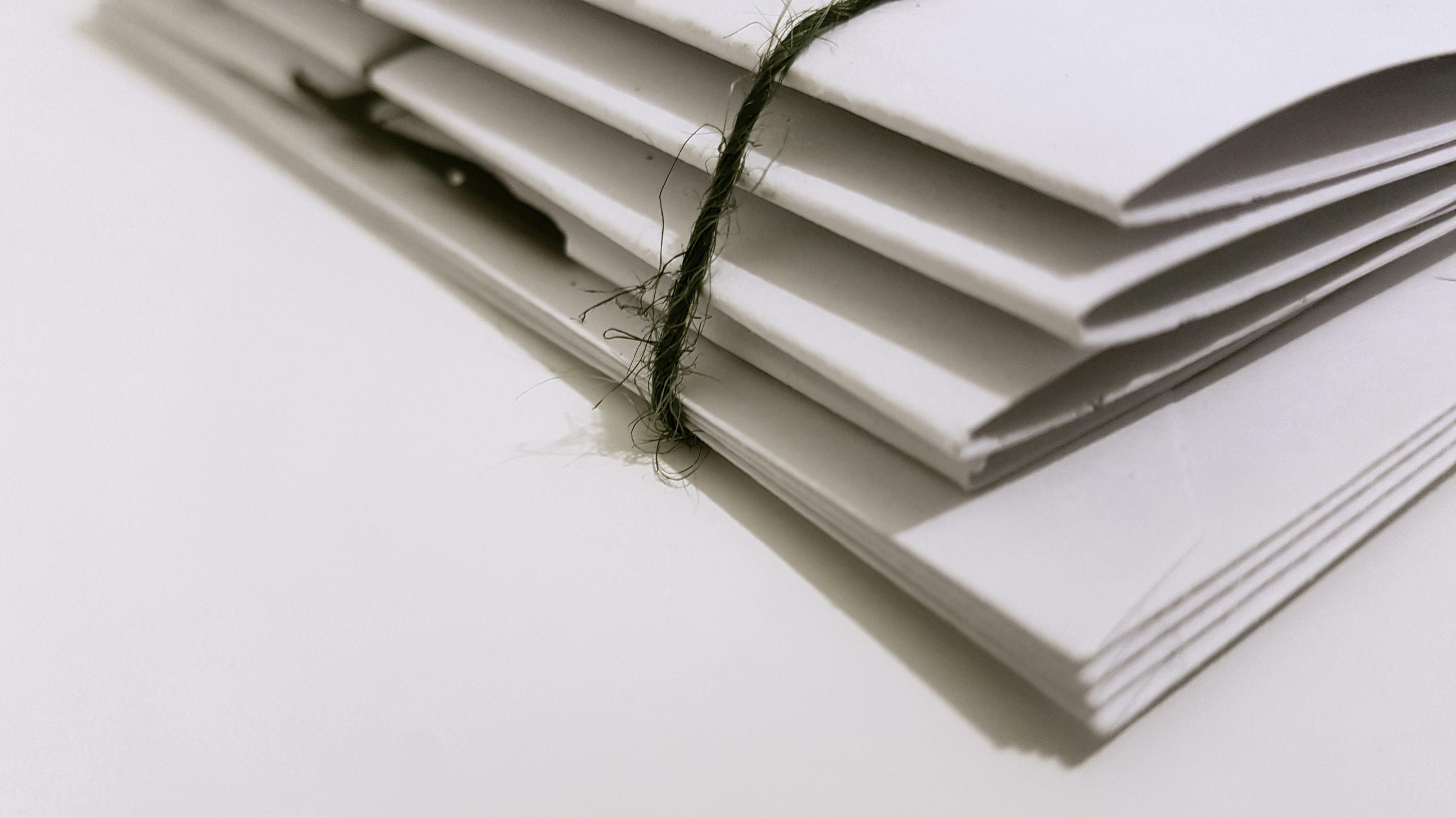 Ein dünner Stapel Papierakten, der mit einer grünen Korden zusammengebunden wurde. Die Perspektive ist von schräg unten auf die auf einer Fläche liegenden Unterlagen.