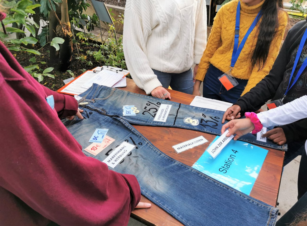 Studierende führen im Tropenschauhaus einen Workshop mit Schüler*innen durch. Darin geht es um Baumwolle und die Wertschöpfungskette einer Jeans.