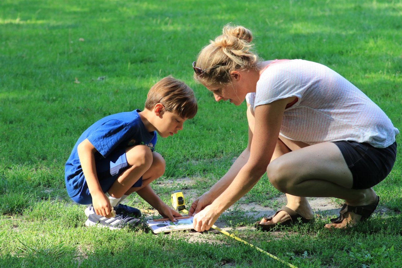 Ein Grundschulkind und eine Naturpädagogin entdecken gemeinsam in der Hocke sitzend Natur im Park.