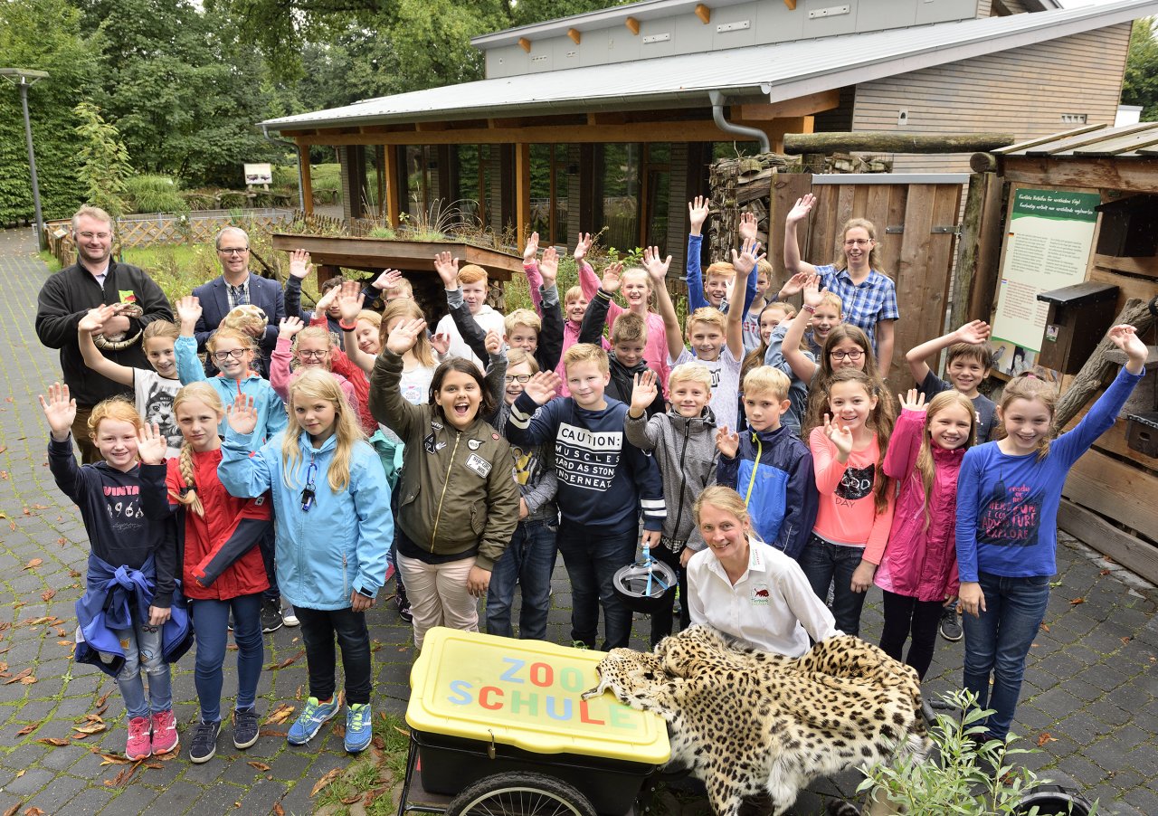Das Bild zeigt eine Schulklasse, die mit Freude an einer Führung teilnimmt. Zu sehen sind auch eine Schlange und ein Leopardenfell.