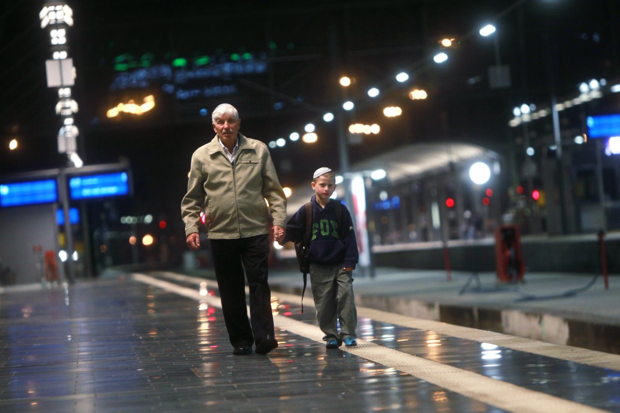 Großvater mit seinem Enkel, der Kippa trägt, geht am Abend einen Bahnsteig entlang.