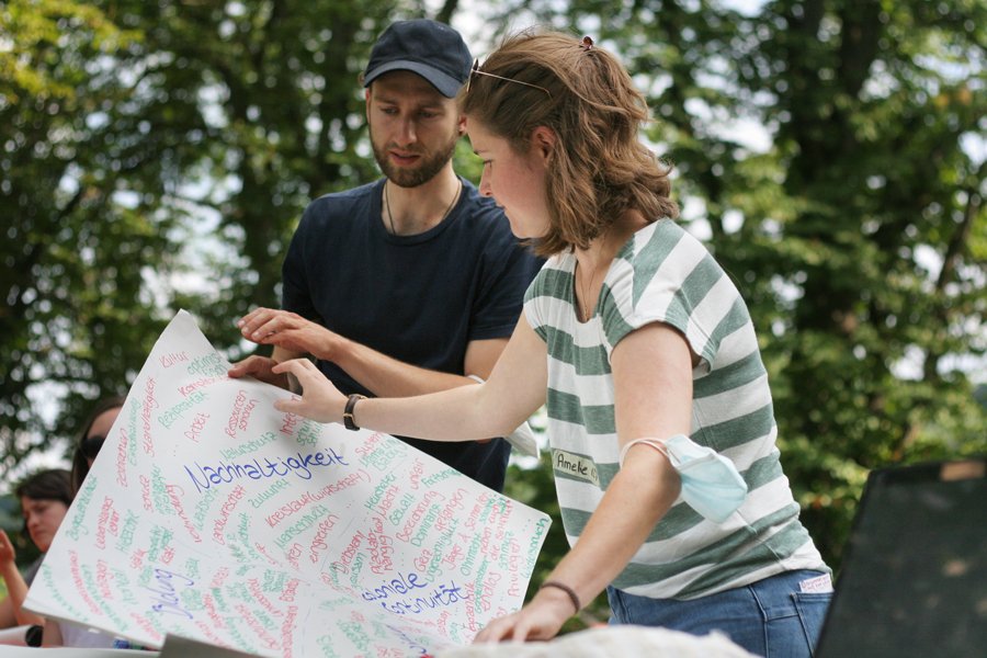 junge Frau zeigt auf ein Plakat, auf dem Nachhaltigkeit steht. Junger Mann hält das Plakat und zeigt ebenfalls darauf.