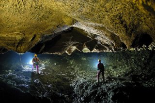 Zwei Personen stehen in einer weitläufigen Höhle und leuchten mit Taschenlampen in die Höhle.