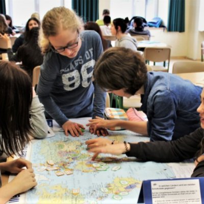 Schülerinnen studieren eine auf dem Tisch ausgebreitete Weltkarte