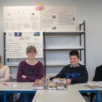 Schülerinnen und Schüler der UNESCO-AG der Heinrich Böll Schule sitzen vor selbst angefertigten Plakaten